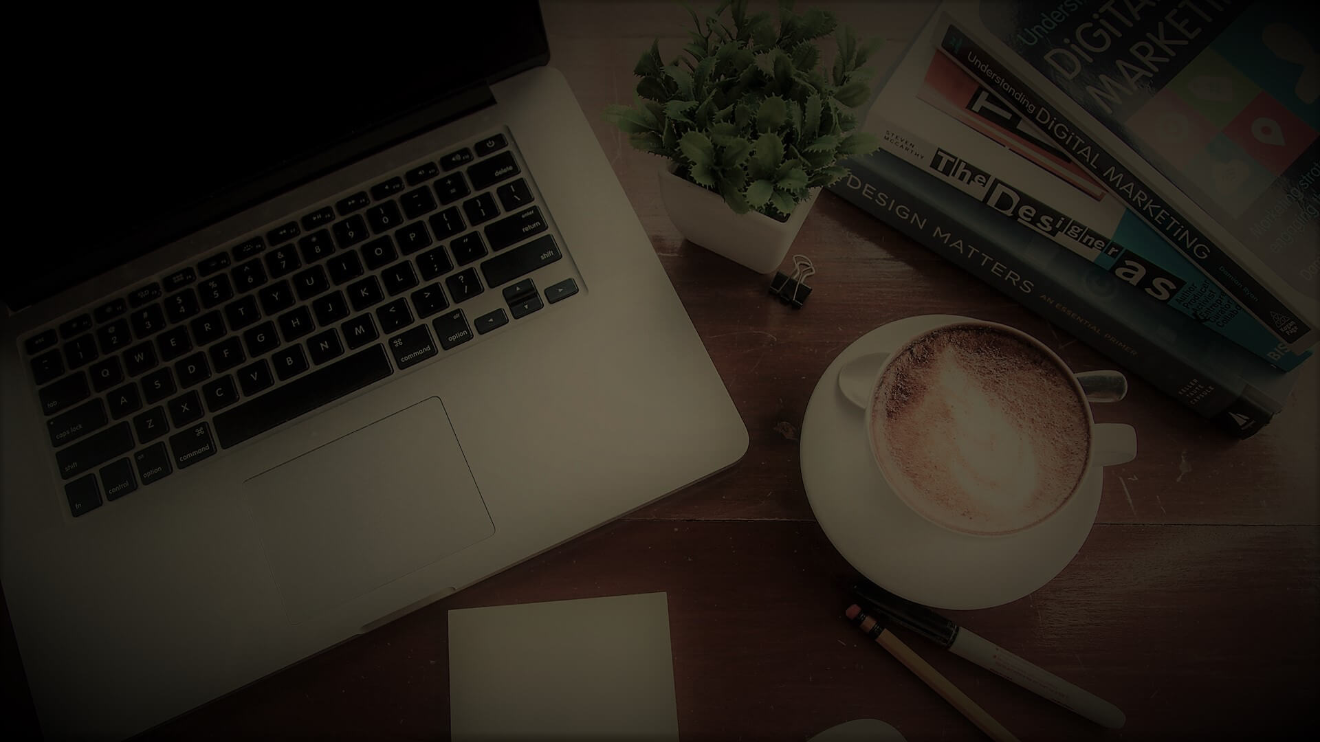 un ordinateur portable, un café, des livres, un cayon, un stylo, et une petite plante sur un bureau