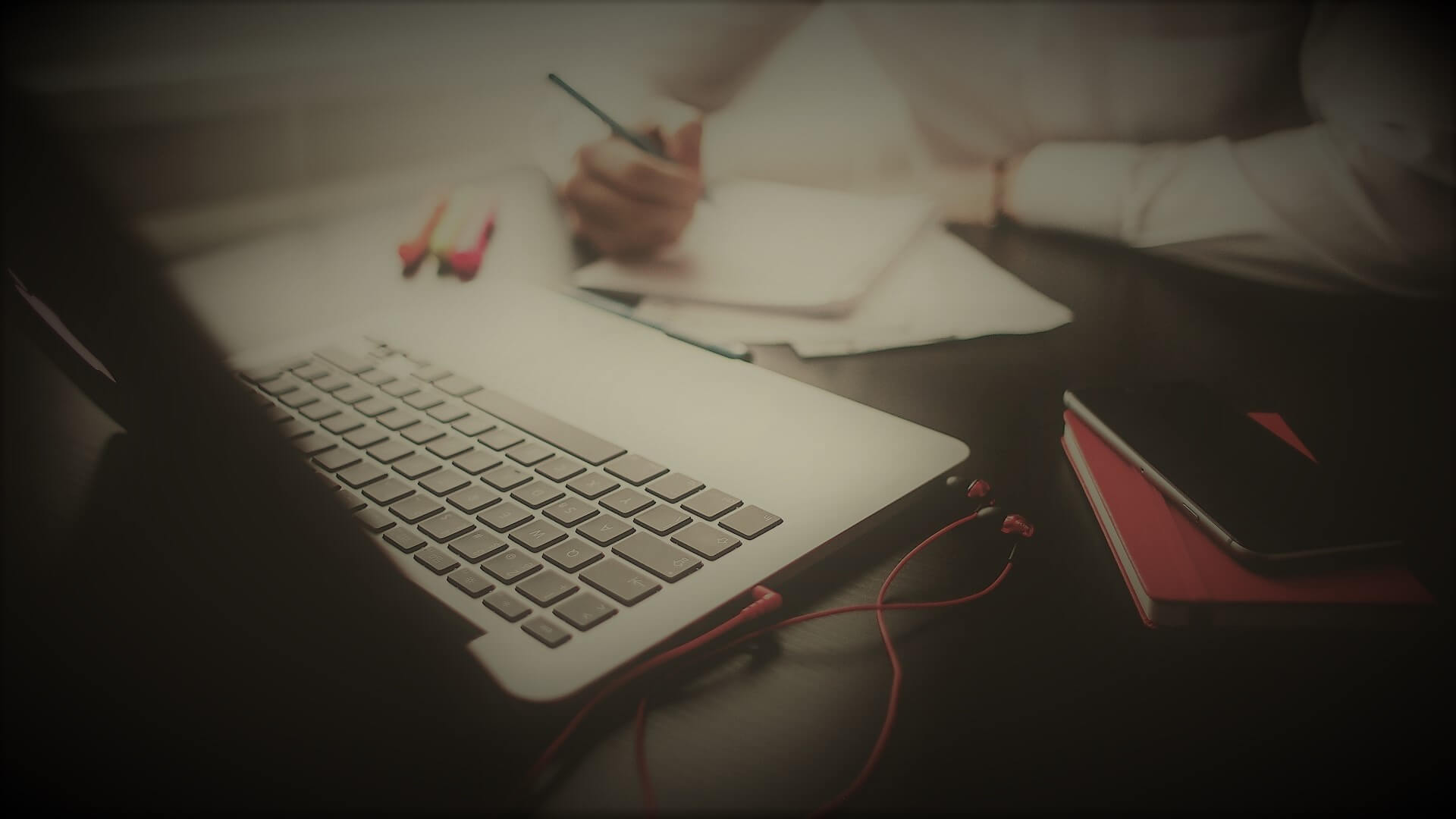 un developpeur devant son ordinateur protable qui tient un stylo dans sa main droite et qui pense a écrire sur son cahier